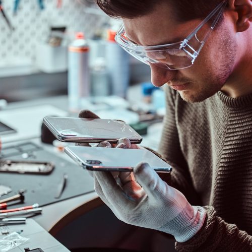 Electronic technician holds two identical smartphones for comparison, in one hand broken and in another new